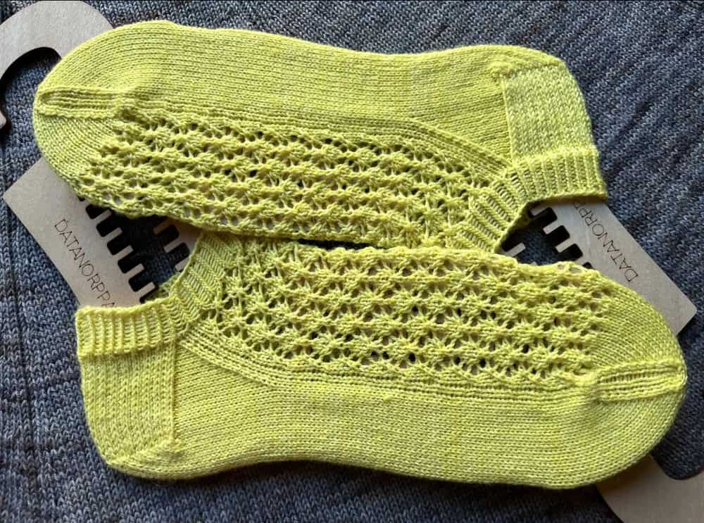 Two bright yellow hand-knitted ankle socks with an openwork lace pattern, each stretched over a wooden sock blocker.